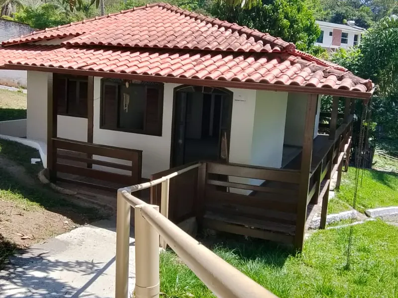 Chalé branco de telhado cerâmico com varanda de madeira, rampa com corrimão e gramado em volta