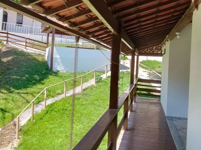 Varanda coberta com telhado de madeira e piso de tábuas, ao lado de um gramado em declive